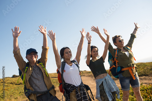 Family of backpackers raising arms and smiling outdoors. Excited parents with teen daughters hiking in summer. Active family weekend concept