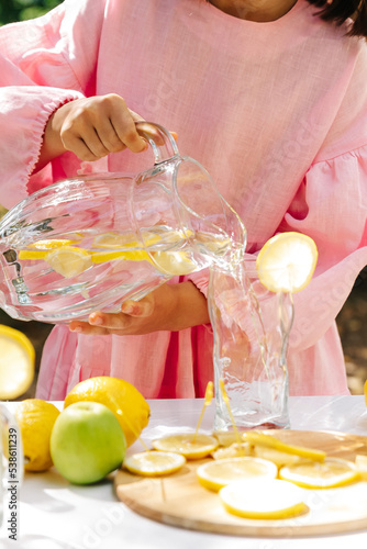 a girl in a pink dress pours homemade lemonade into a glass