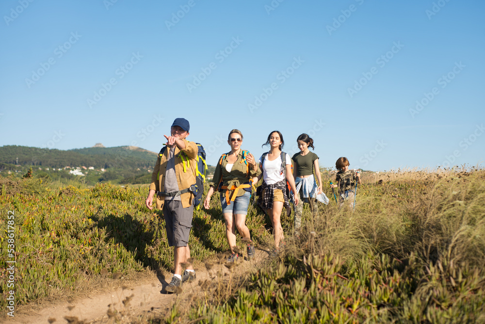 Happy family of backpackers following their father. Man showing direction to wife and children when hiking in mountain. Active family weekend concept