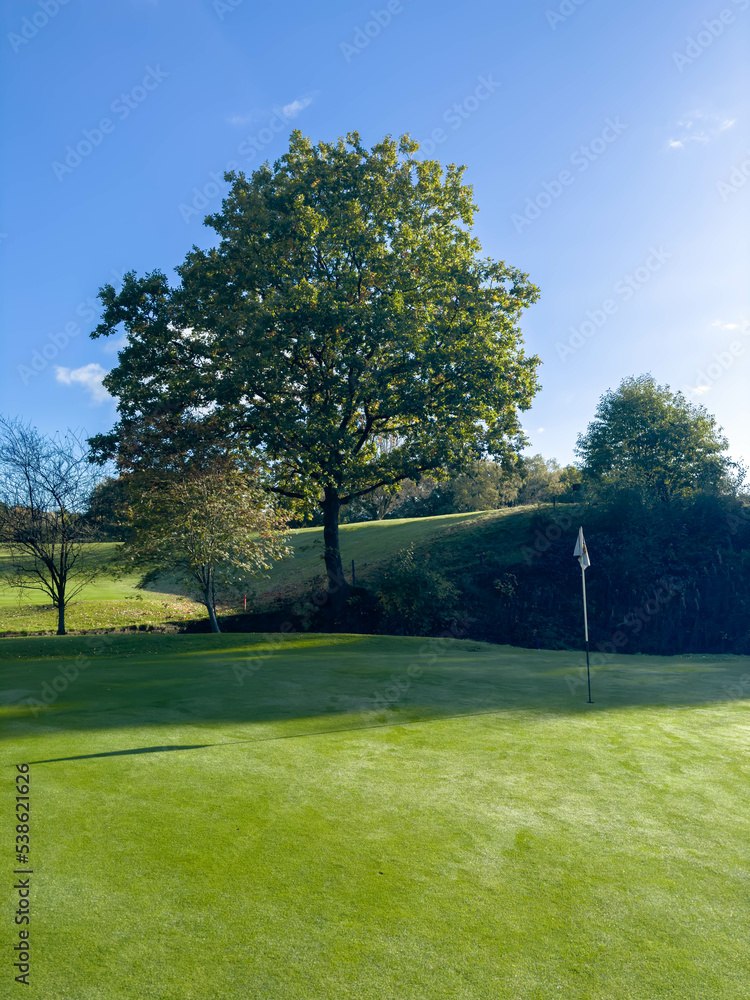 Golf Course green with blue sky and flag in view, autumn day with dew