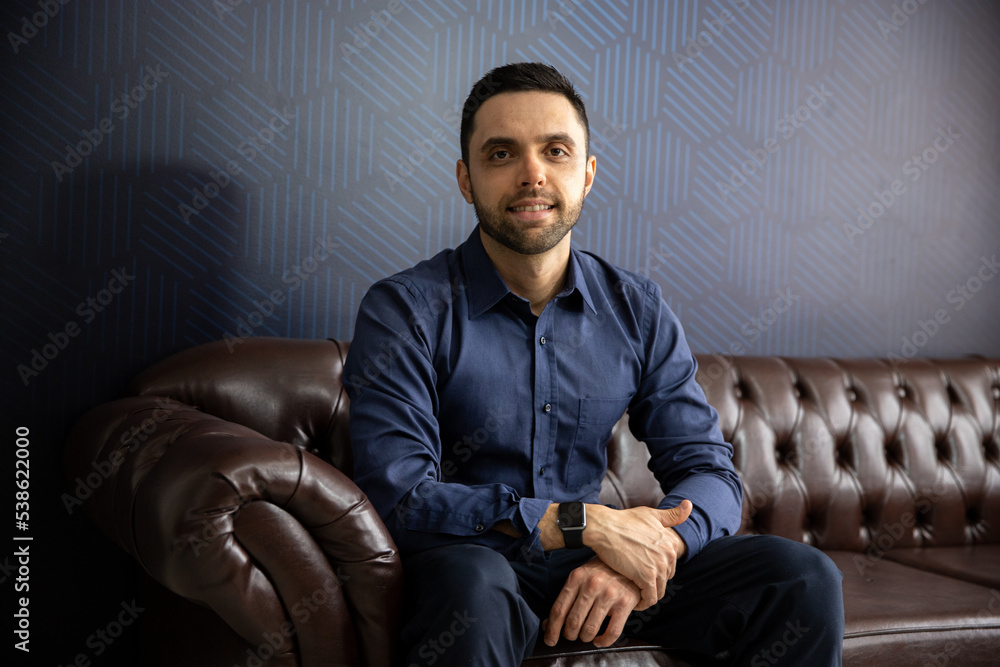 portrait man sitting on a sofa looking at camera and smiling, businessman in his office, technology entrepreneur portrait man sitting on a sofa looking at camera and smiling, businessman in his office, technology entrepreneur