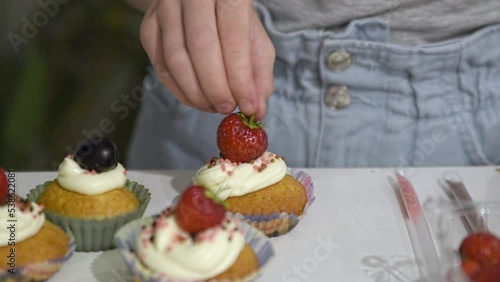 A Caucasian girl decorates cupcakes with strawberries