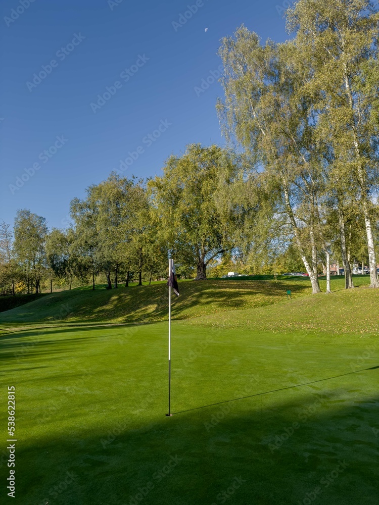 Obraz premium Golf Course green with blue sky and flag in view, autumn day with dew