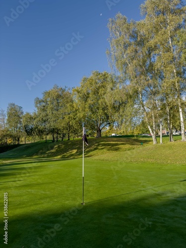 Golf Course green with blue sky and flag in view, autumn day with dew