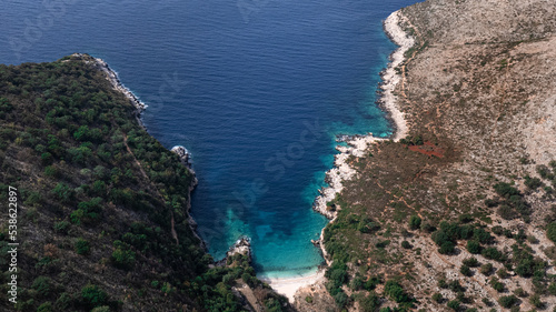 View from above of a bay with blue and turquoise water and a beach, surrounded by hills in Albania