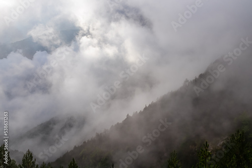 Panoramic view of foggy alpine valley on the hiking trail leading to Mount Olmypus, Macedonia, Greece, Europe. Mountain ranges are heavily covered in mystical early morning clouds and fog. Wanderlust