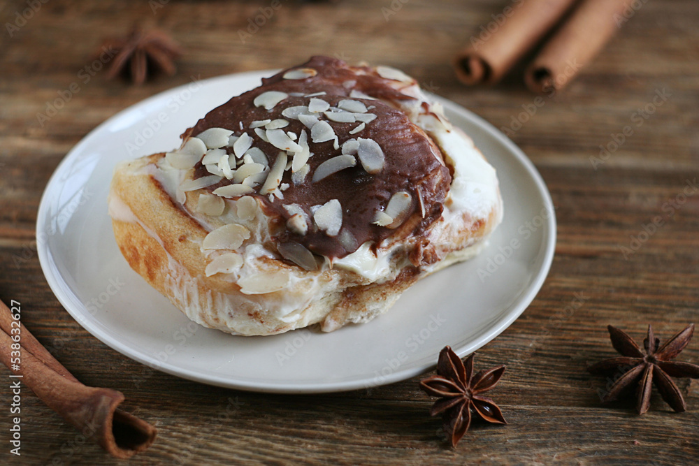 Brioche bun lies in a plate on a wooden table. Nearby are cinnamon sticks and star anise. Brioche bun lies in a plate on a wooden table. Nearby are cinnamon sticks and star anise.