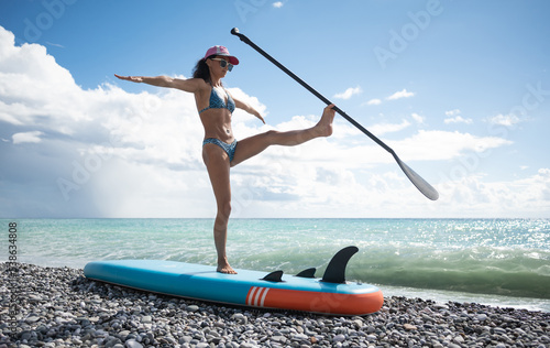 a sporty girl in a swimsuit with a paddle poses sexually with a sup board in summer against the background of the sea