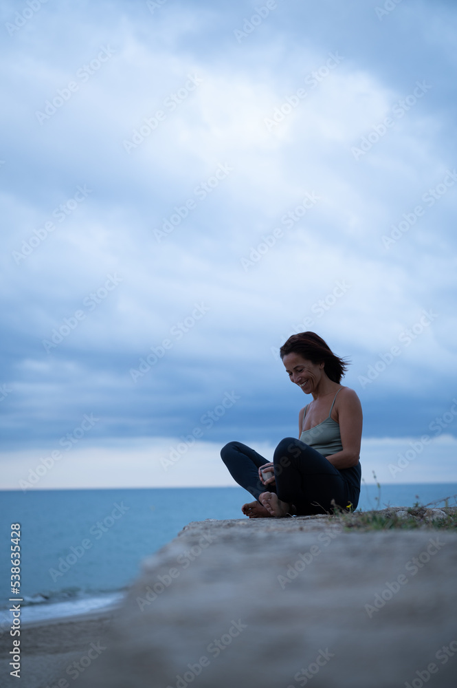 Side view of woman sitting relaxed and smiling after doing a yoga session.