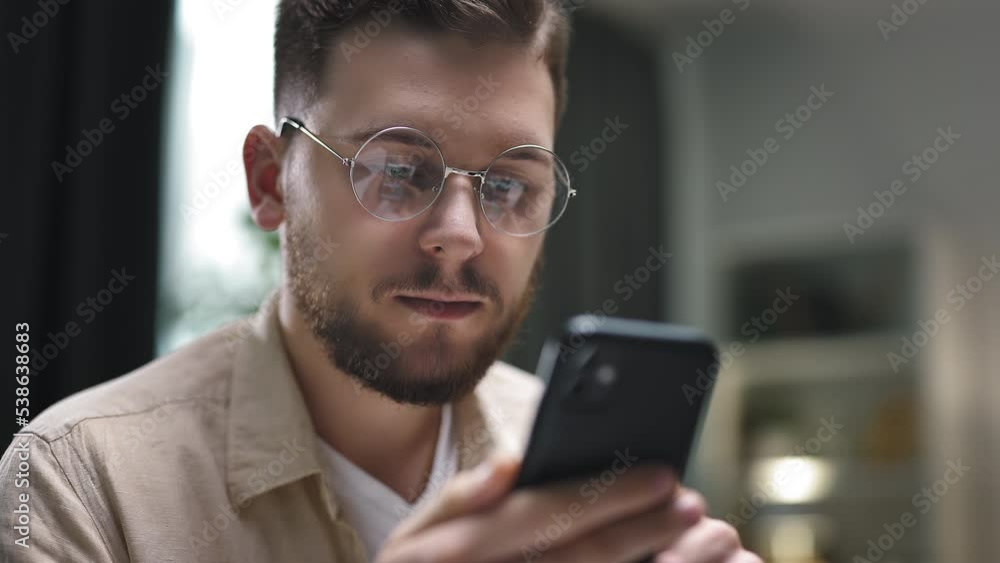 Young caucasian male in round eyeglasses scrolling smartphone, checking social media and e-mail. Young caucasian male in round eyeglasses scrolling smartphone, checking social media and e-mail.