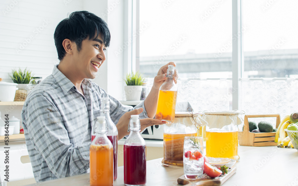 Portrait handsome man smiling with fresh and happiness, holding glass of Kombucha healthy fermented probiotic tea drinks with ingredients red apples, strawberries, mushroom scoby in kitchen at home. Portrait handsome man smiling with fresh and happiness, holding glass of Kombucha healthy fermented probiotic tea drinks with ingredients red apples, strawberries, mushroom scoby in kitchen at home.