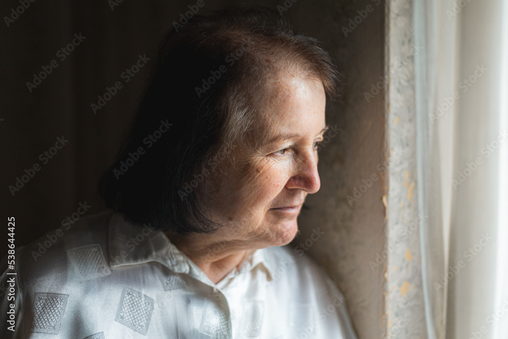 Elderly woman standing and looking through the window Elderly woman standing and looking through the window