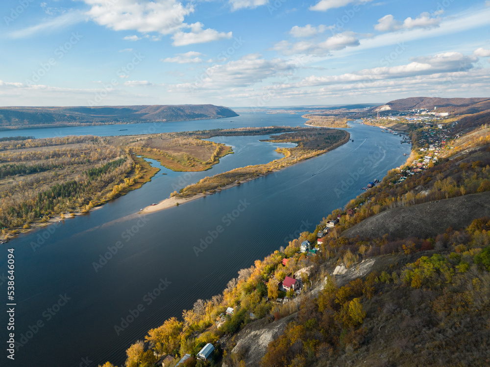 The concept of an ecological village. A village on the riverbank with a view of an island in the middle of the river and mountains, a view from a drone. Aerial photography of autumn. Golden Autumn