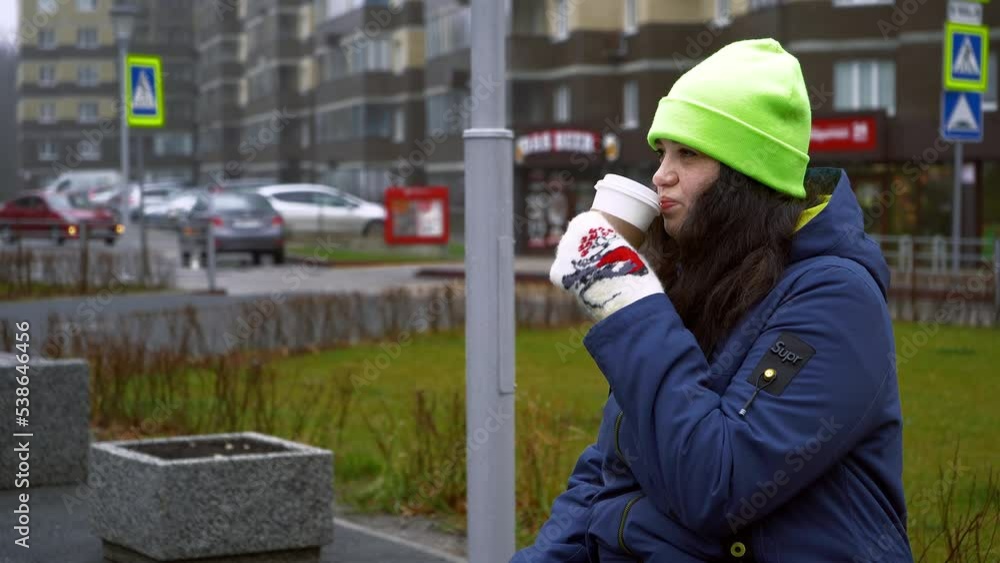 A girl drinks coffee in the park. The girl is sitting on a bench and drinking coffee in winter. The girl is cold. Hot coffee in the hands of a girl. A girl drinks coffee in the park. The girl is sitting on a bench and drinking coffee in winter. The girl is cold. Hot coffee in the hands of a girl.