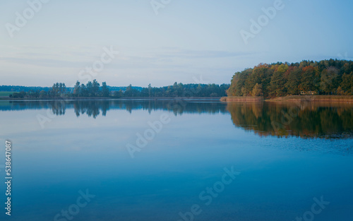 Beautiful sunset, sky with clouds over the lake. Reflection of the autumn landscape in the water surface.