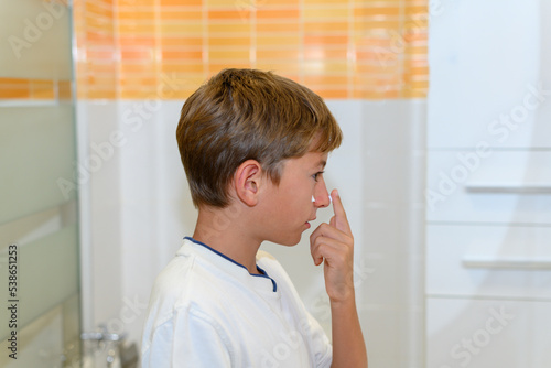 Preteen puts cream on her face in the toilet. Side view. Concept of skin care