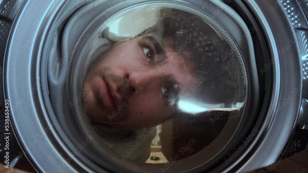 Young man looks into a laundry washing machine. view from inside. Young man looks into a laundry washing machine. view from inside.