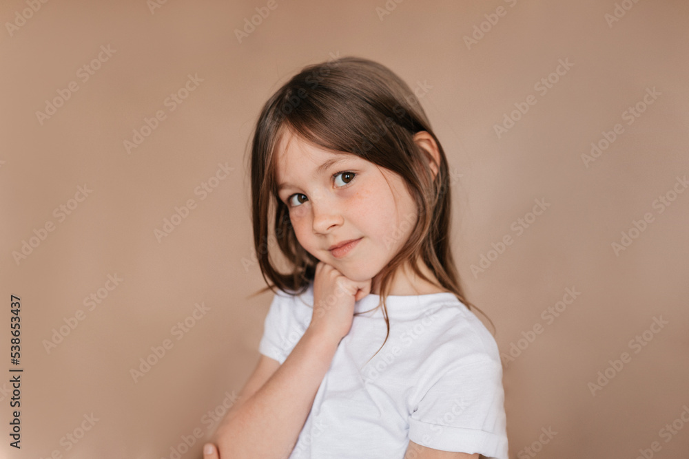 Stylish pretty charming girl with dark hair wearing white t-shirt posing at camera with charming smile over isolated beige background Stylish pretty charming girl with dark hair wearing white t-shirt posing at camera with charming smile over isolated beige background