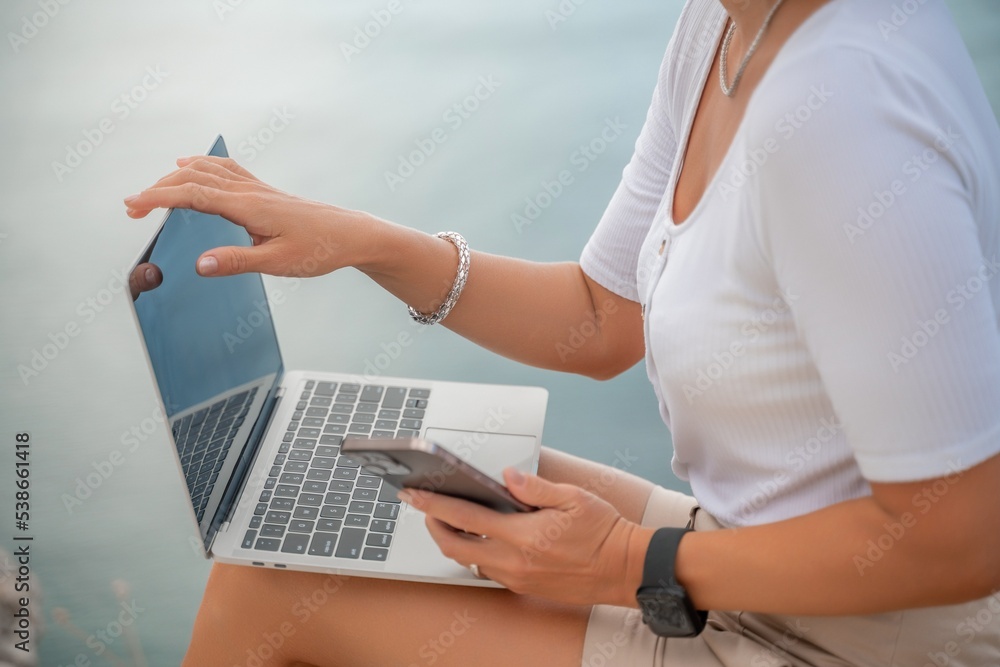 Naklejka premium Freelance close up woman hands writing on computer. Well looking middle aged woman typing on laptop keyboard outdoors with beautiful sea view.
