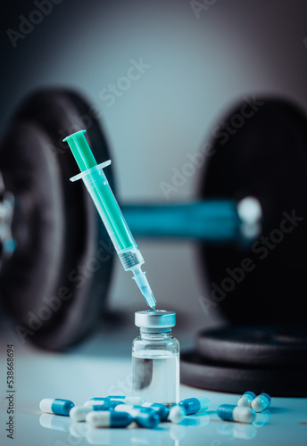 Closeup of illegal doping injectable drug and capsules and weight plates - cheating drug in sports