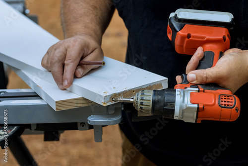 Using screwdriver, he drills holes in wooden boards in order to connect them together so that they can be used for construction purposes photo