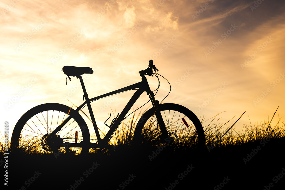 silhouette of a bicycle in the grass against an orange sky during sunset silhouette of a bicycle in the grass against an orange sky during sunset