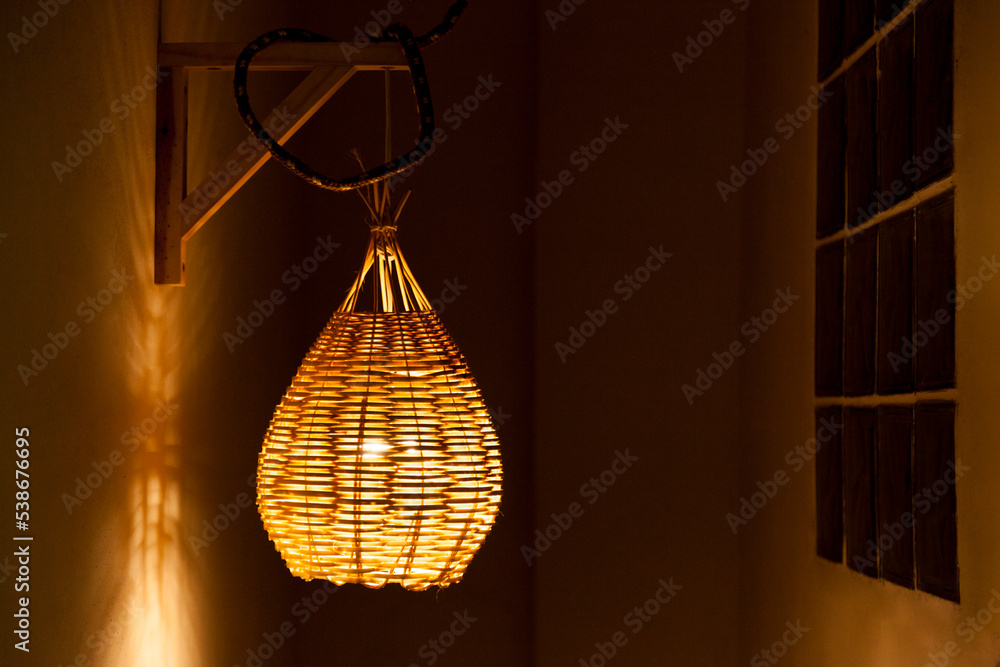 Pendant luminaire for outdoor area with yellow light. Handmade lamp made of straw. Luminaire concept. Home sweet home concept.