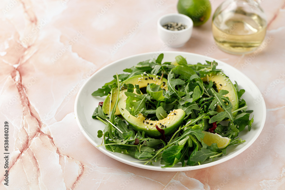 Diet green salad with avocado and mix lettuce, arugula on white plate and beige marble background.