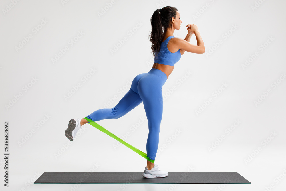 Fototapeta premium Fitness woman doing exercise for glutes with resistance band on gray background. Athletic girl working out.