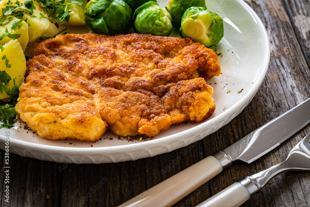Breaded fried pork chop with boiled potatoes and brussels sprouts  on wooden table
