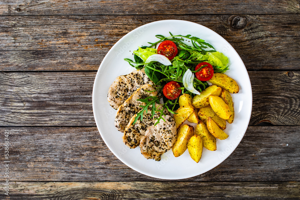Fried pork loin with baked potatoes and fresh green vegetables on wooden table
Fried pork loin with baked potatoes and fresh green vegetables on wooden table