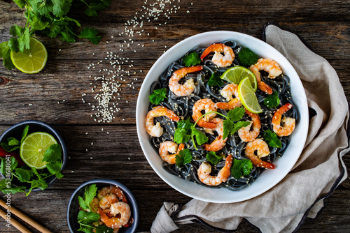 Black rice noodles with fried prawns and coriander on wooden table 