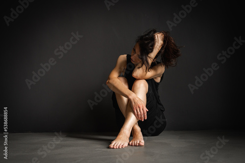 young pretty girl sitting on the floor, pensive, thinking, depression, dark background, low key