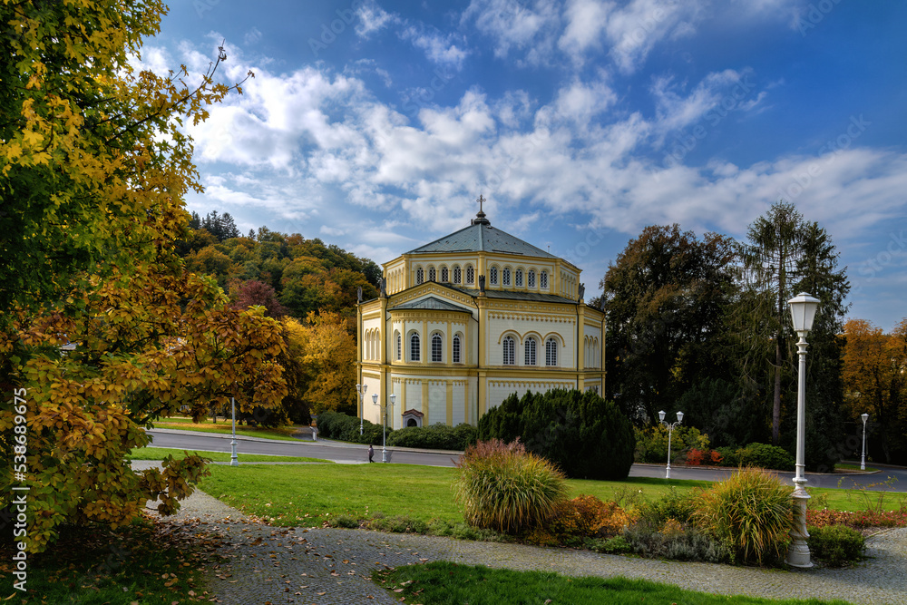 Marianske Lazne (Marienbad) - Catholic Church of the Assumption of the Virgin Mary in the Czech spa town in autumn - blue sky and trees with colourful leaves