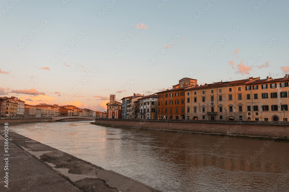 Beautiful cozy European town with colorful houses along the river with a bridge at sunset in Pisa, Italy
