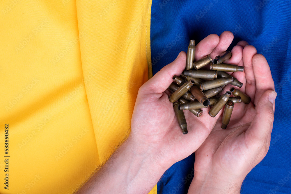 holds hryvnia banknotes and bullet casings in his hands on a background divided by half by a blue and yellow Ukrainian flag. concept of buying weapons from other countries