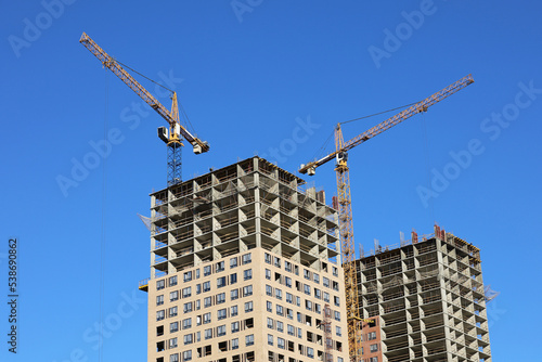 Tower cranes and unfinished buildings on background of blue sky. Housing construction, apartment blocks in city