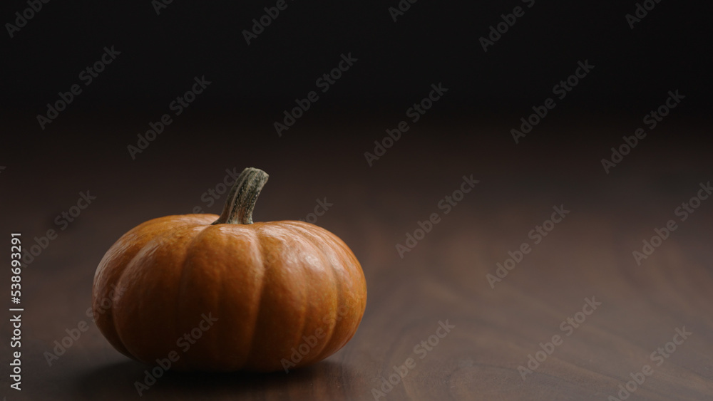 small orange pumpkin on walnut table with balck wall and