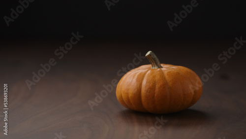 small orange pumpkin on walnut table with balck wall and