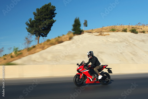 Side view of a motorcycle rider riding red race motorcycle on the highway with motion blur.