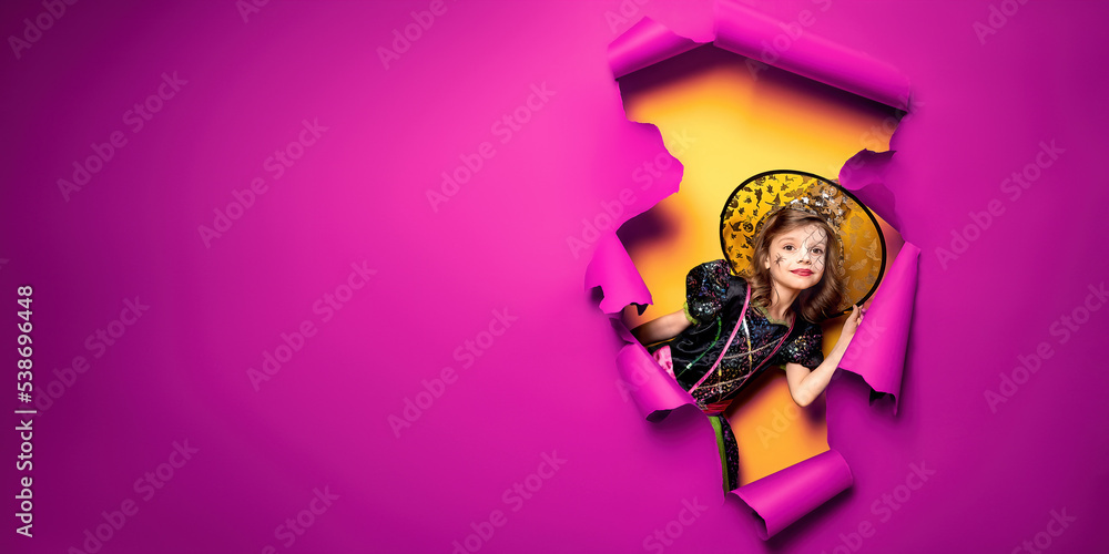 a little girl in a witch costume peeks out of a hole in a paper background