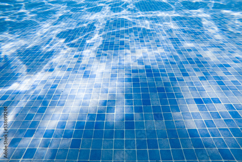 Blue tiled floor inside underwater swimming pool with light difraction effect