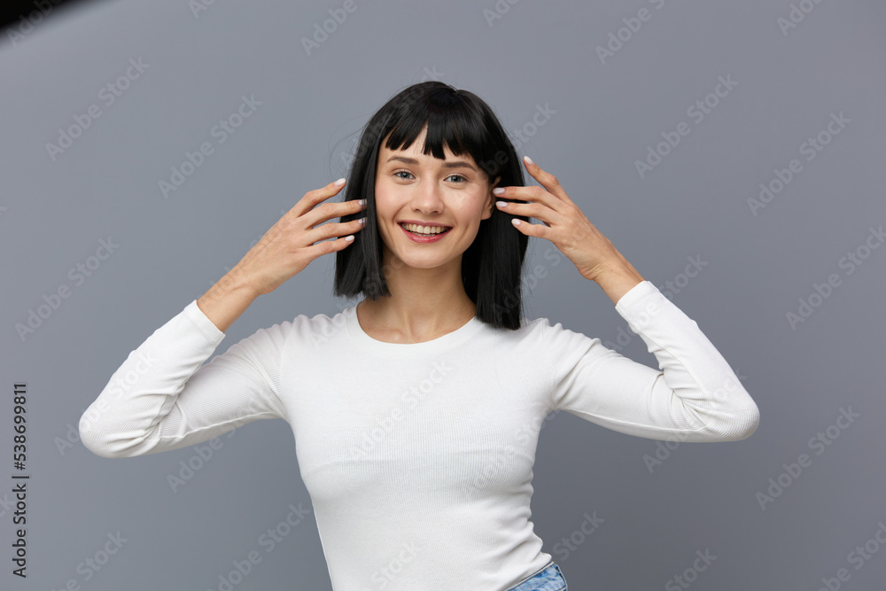 a calm woman stands against a dark background in a tight white T-shirt, elbows apart in different directions, straightening her hair a calm woman stands against a dark background in a tight white T-shirt, elbows apart in different directions, straightening her hair