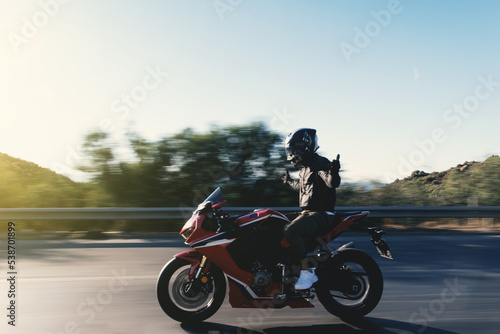 Fototapeta Naklejka Na Ścianę i Meble -  Side view of a motorcycle rider riding red race motorcycle on the highway with no hands and with motion blur.