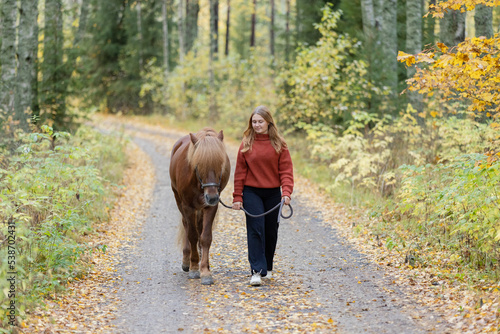Young woman walking on gravel road with Icelandic horse in autumn scenery. © AnttiJussi
