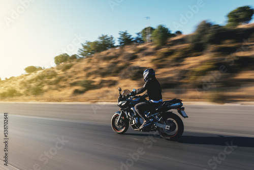 Fotografiet Side view of a motorcycle rider riding on the highway with motion blur