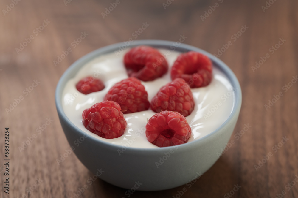 Yogurt with fresh raspberries in blue ceramic bowl on walnut table Yogurt with fresh raspberries in blue ceramic bowl on walnut table