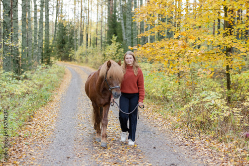 Young woman walking on gravel road with Icelandic horse in autumn scenery.