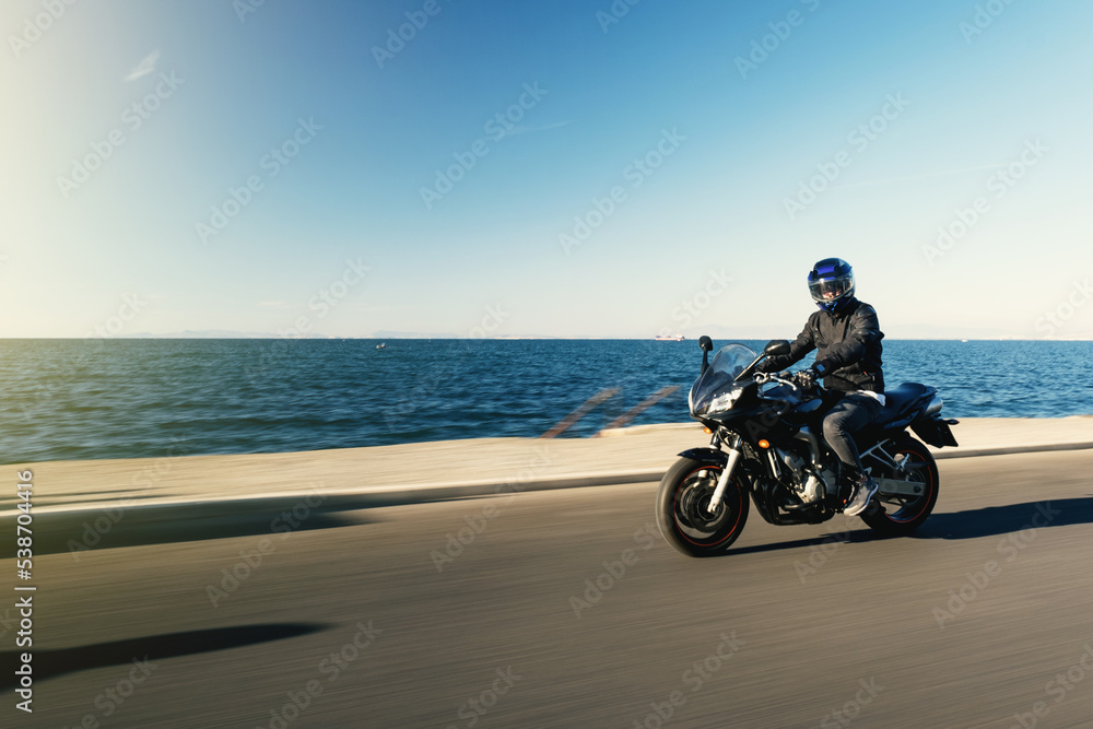 Side view of a motorcycle rider riding race motorcycle on a sea background with motion blur Side view of a motorcycle rider riding race motorcycle on a sea background with motion blur