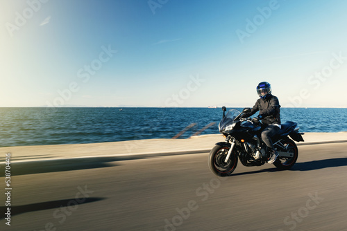Side view of a motorcycle rider riding race motorcycle on a sea background with motion blur